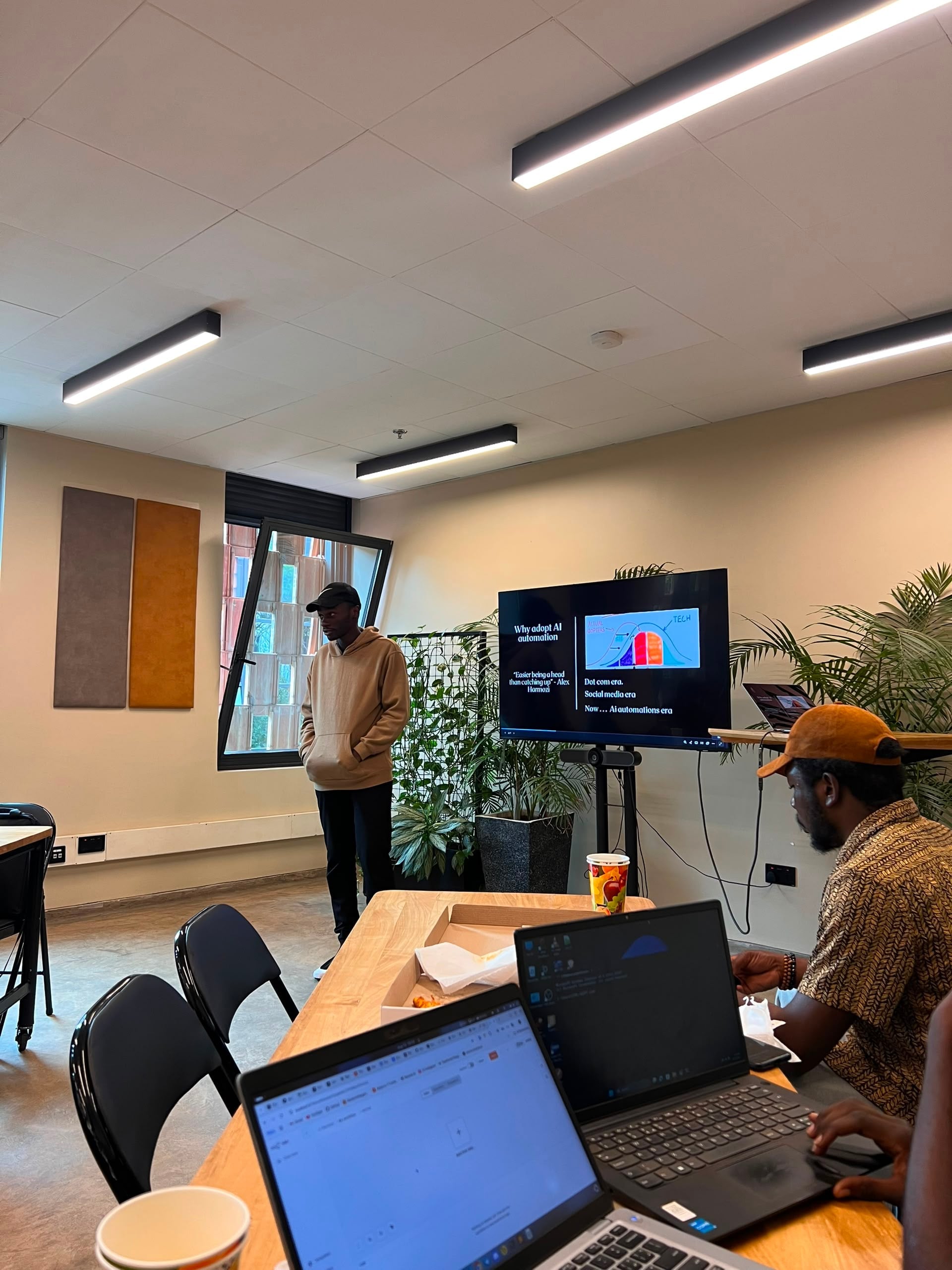 Presenter standing beside a slide titled Why adopt AI automation during an informal office lunch session