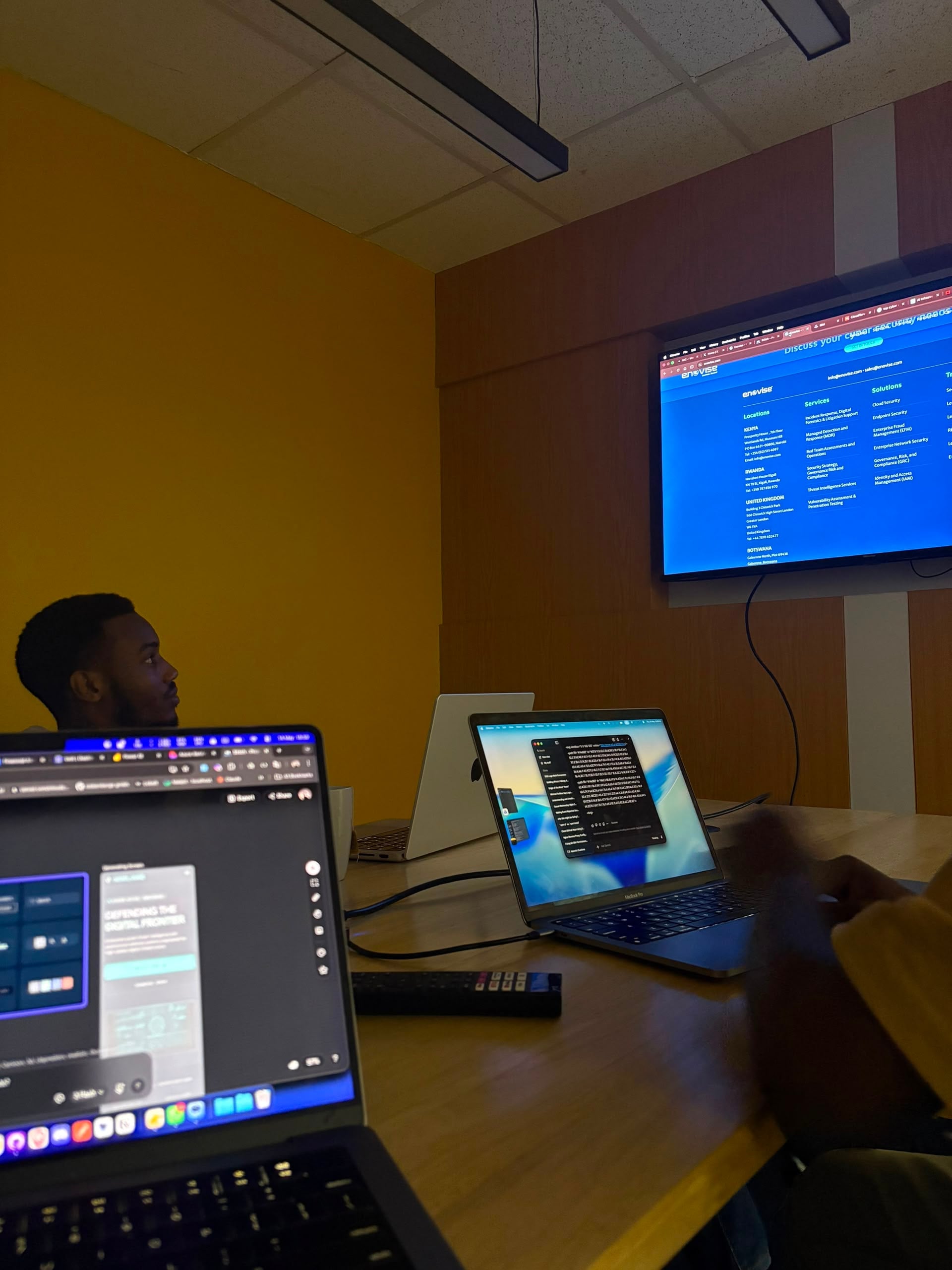Meeting room with laptops open and a wall screen showing an enevise cybersecurity website