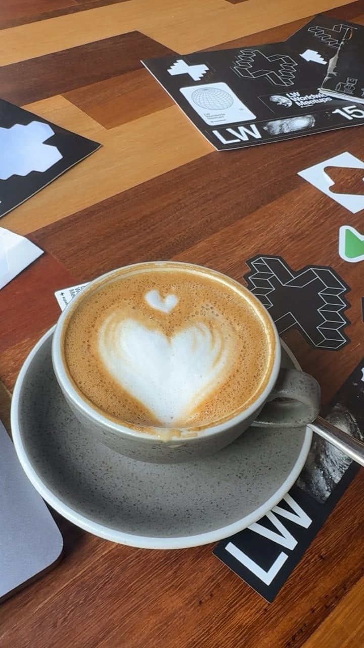Latte with twin heart foam art on a wooden table surrounded by LW stickers
