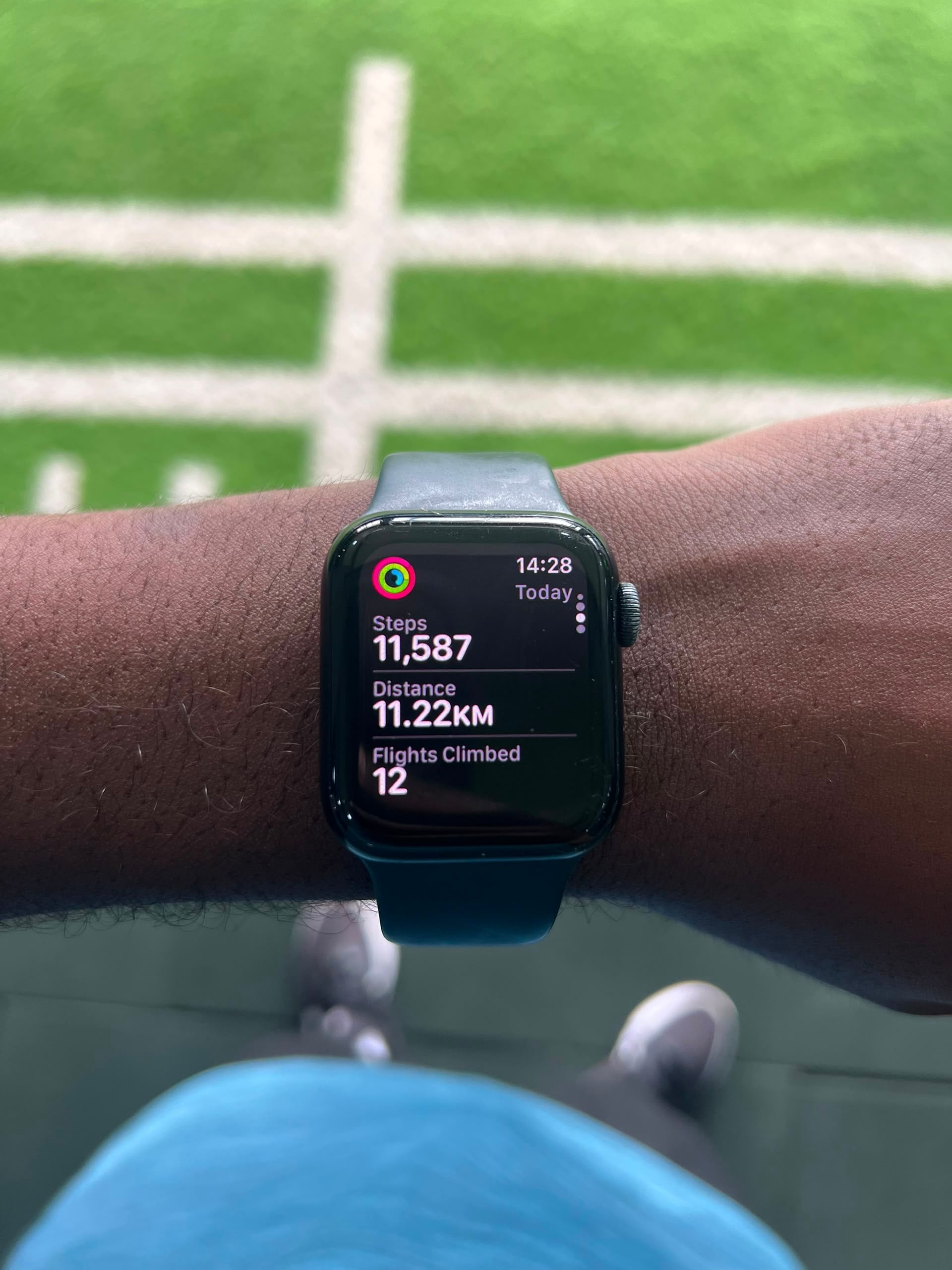 Apple Watch showing 11,587 steps and 11.22 km against a green turf field